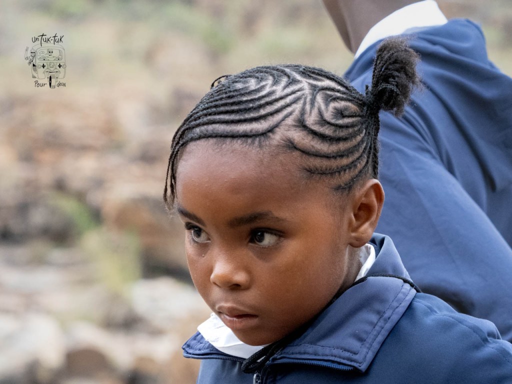 Portrait d'une jeune fille avec des cheveux tressés en motifs, portant une veste bleue.