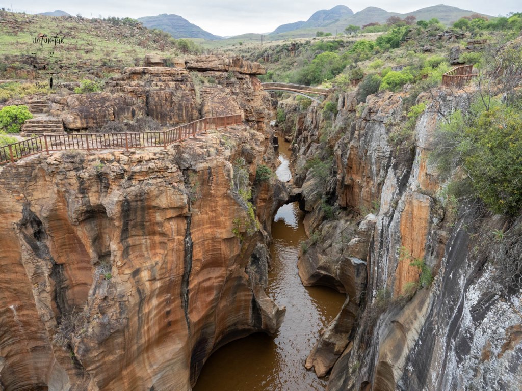 Vue panoramique d'un canyon avec des parois rocheuses et une rivière serpentine, entouré de verdure et de collines en arrière-plan.