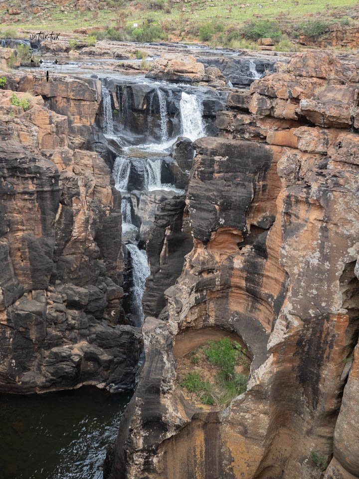 Vue d'une cascade se déversant dans un canyon étroit entouré de roches couleur terre et de verdure.