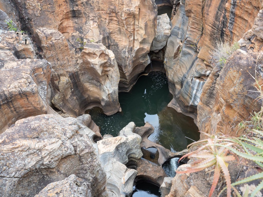 Vue plongeante sur des formations rocheuses et un bassin d'eau dans un canyon.