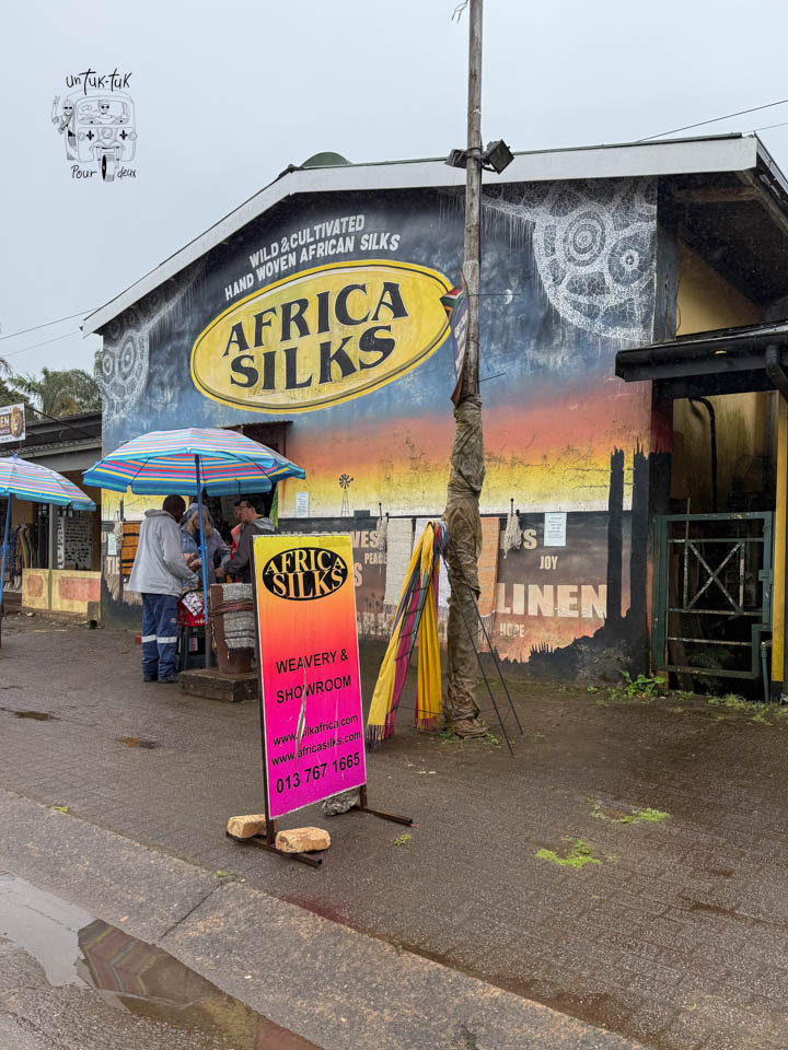 Boutique Africa Silks affichant des soies africaines tissées à la main, avec des clients sous des parasols colorés.