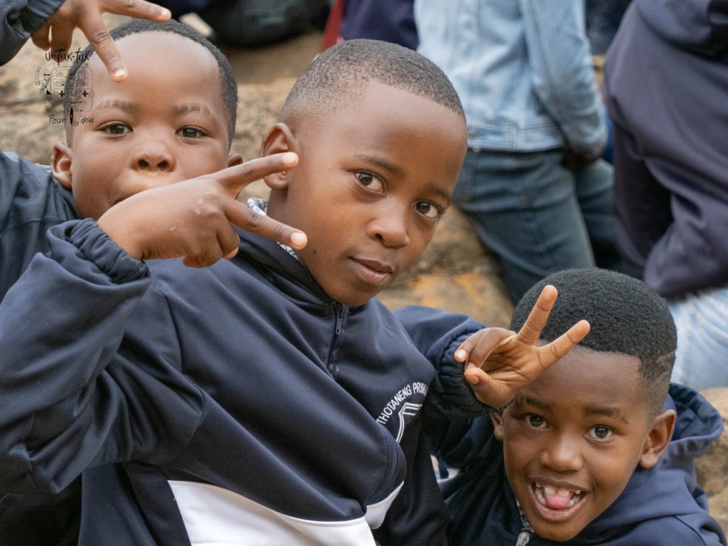 Trois enfants souriants faisant des gestes de paix en portant des vestes de sport.