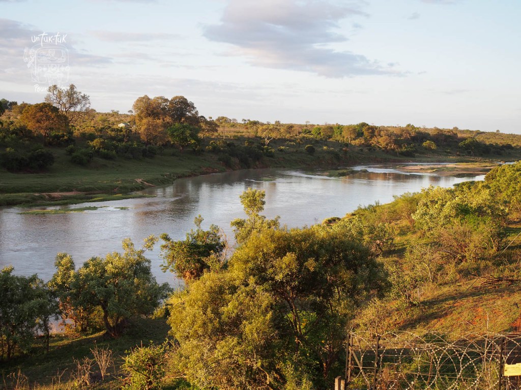 Vue d'une rivière entourée de verdure et de collines sous un ciel légèrement nuageux.