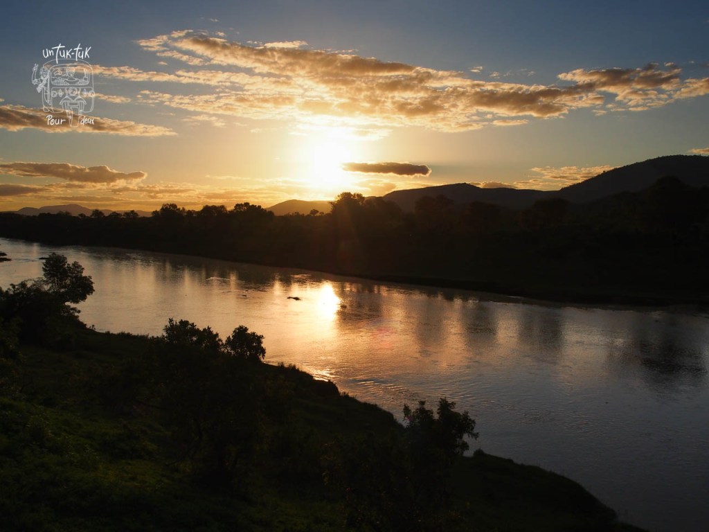 Coucher de soleil sur une rivière avec des montagnes en arrière-plan.