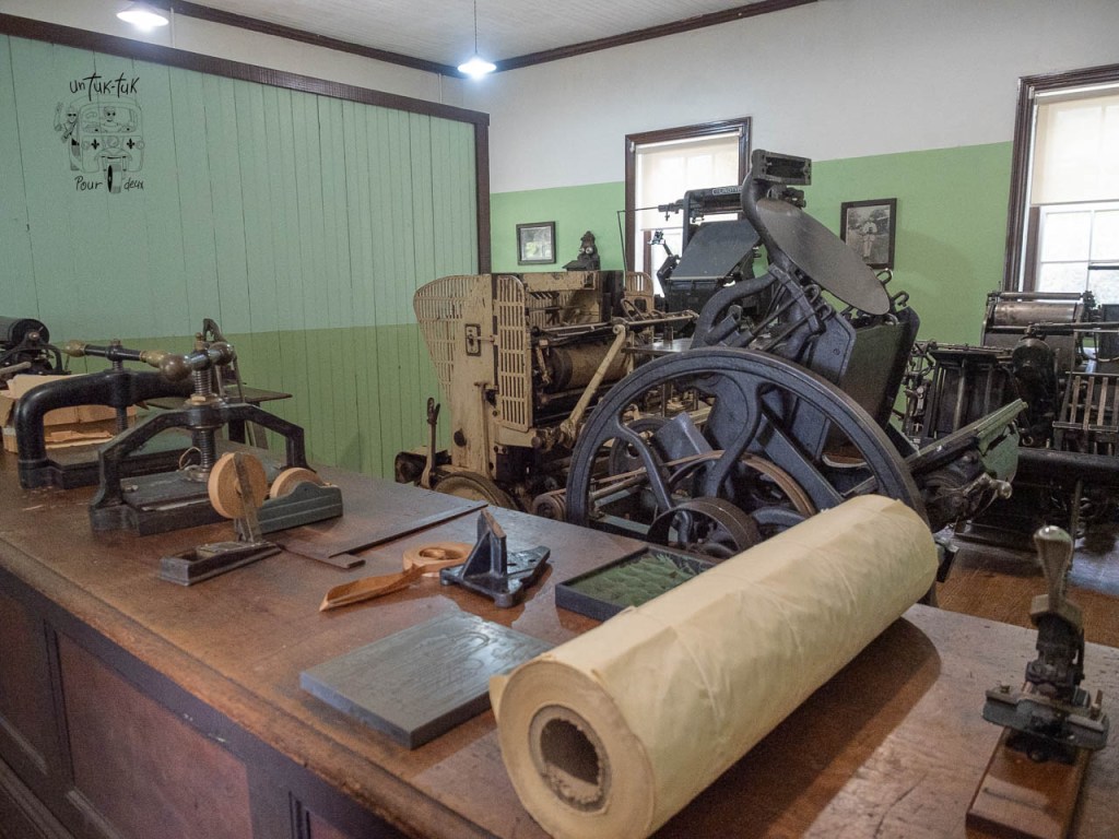 Intérieur d'un atelier d'impression avec des machines anciennes, des outils de gravure et des rouleaux de papier sur une table en bois.